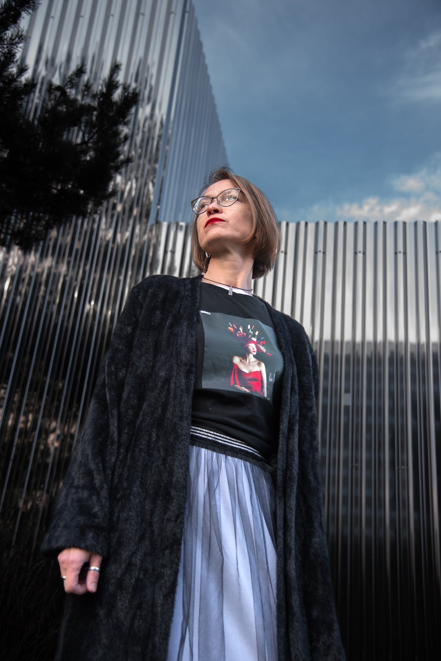 Black unisex T-shirt with AI-generated Hello Weekend print from M2ArtWear, styled with maxi coat and transparent skirt on a model in Zurich